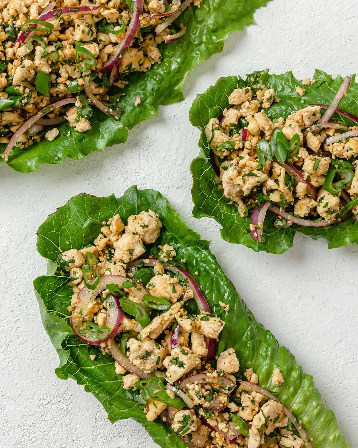 Veganer Tofu-Larb-Salat 2 Drei Portionen Larb Salat auf weißer Oberfläche angerichtet.