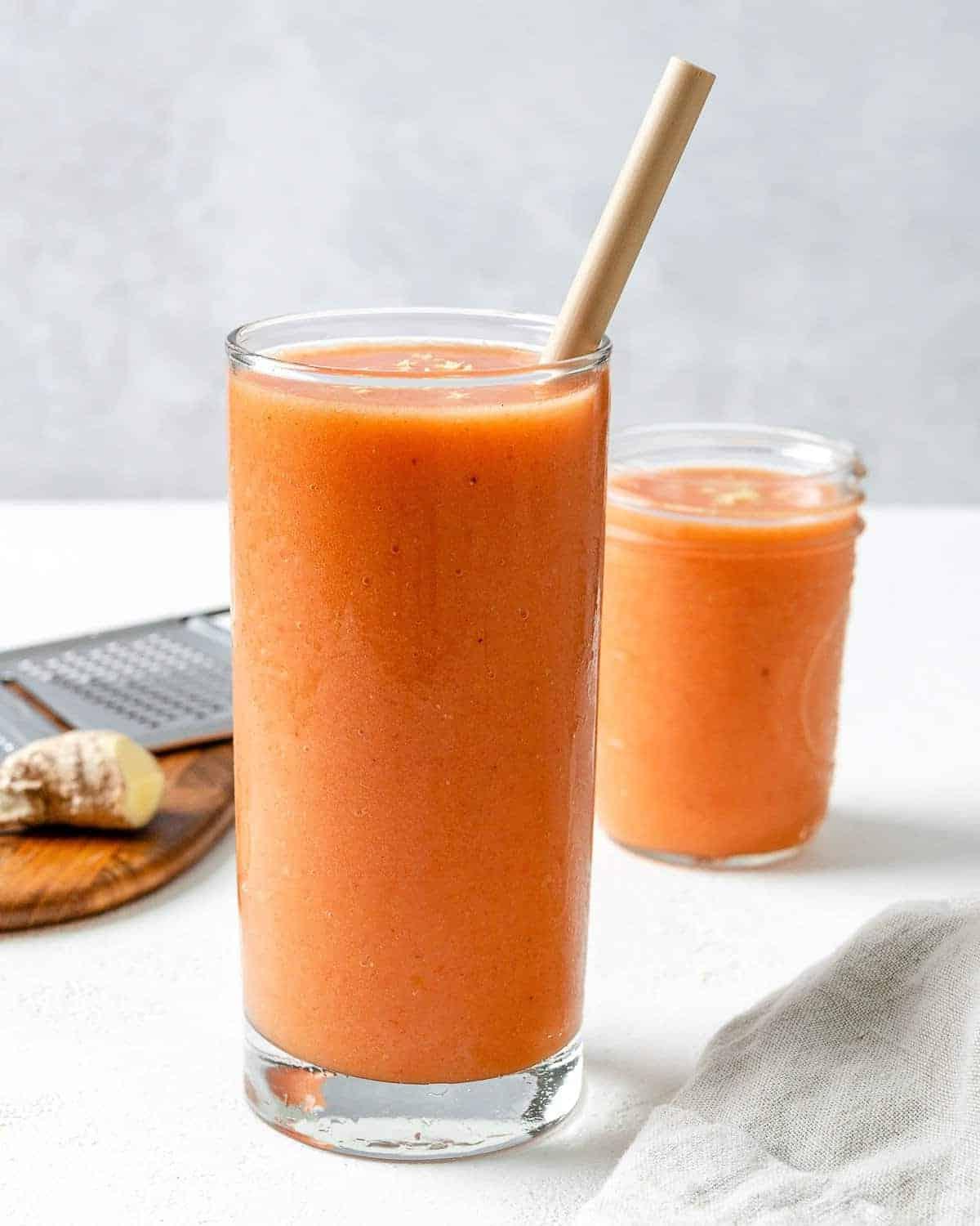 Ingwer-Frucht-Smoothie 2 Fertiger Ingwer-Frucht-Smoothie in einem hohen Glasbecher mit einem Papierstrohhalm im Vordergrund und einem kleinen Glas Smoothie im Hintergrund