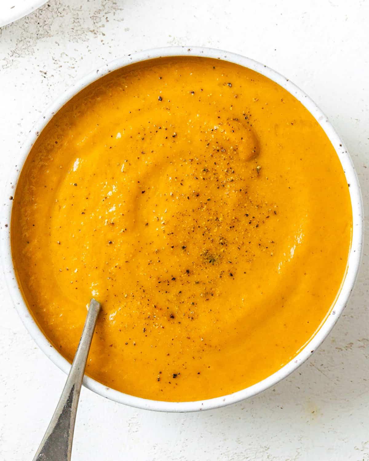 Cremige Curry-Karotten-Ingwer-Suppe 2 Fertige cremige Curry-Karotten-Ingwer-Suppe in einer weißen Schüssel auf weißem Hintergrund.
