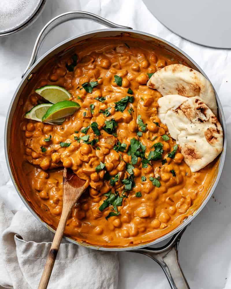 Curry-Kichererbsen 2 Fertiges Kichererbsen-Curry in einer großen Pfanne mit einem Holzlöffel und veganem Naan-Brot daneben.