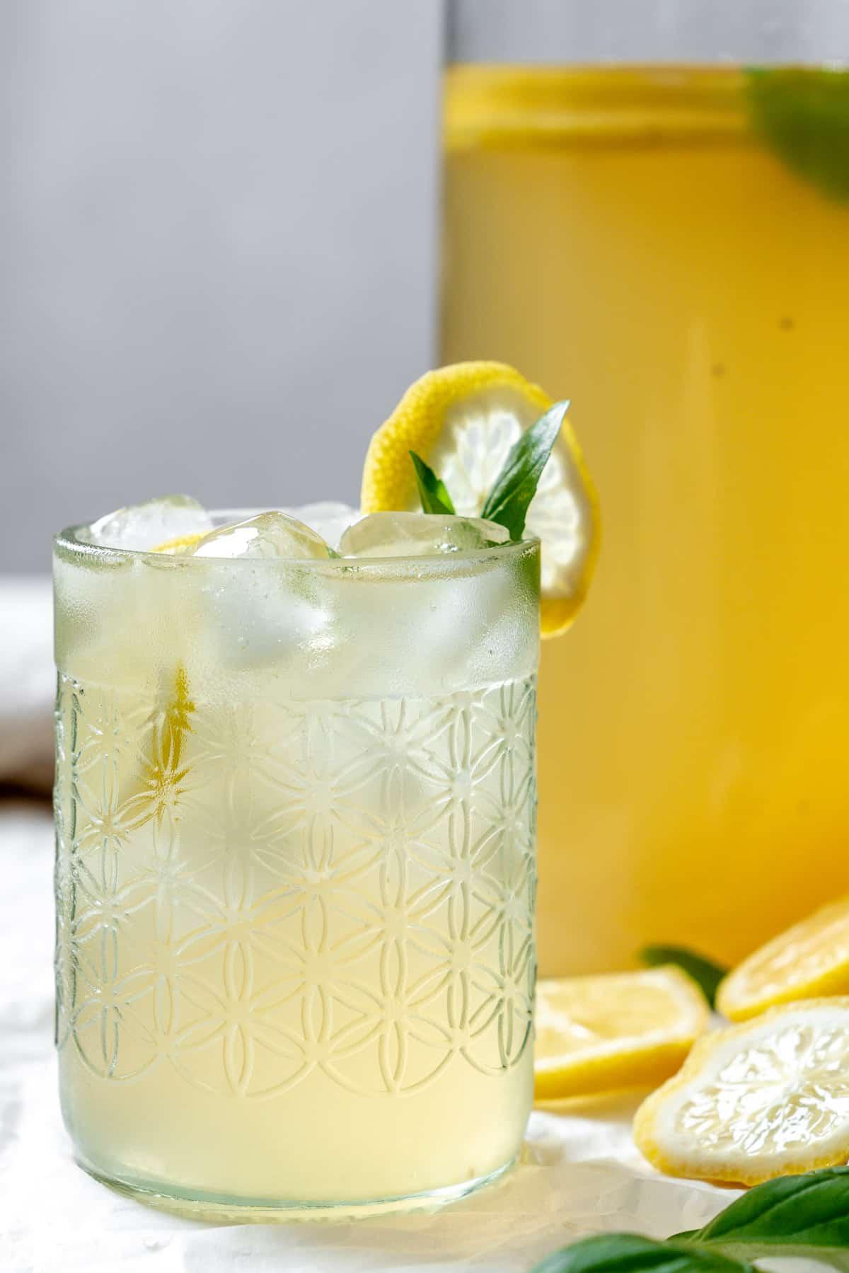 Fertige Basilikum-Limonade in einem Glas mit Zutaten im Hintergrund