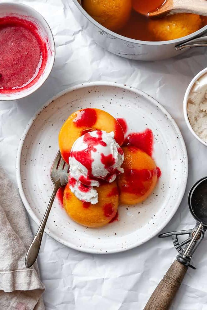 Peach Melba 2 Pochierte Pfirsiche mit Himbeersauce und Eiscreme auf einem Teller angerichtet.