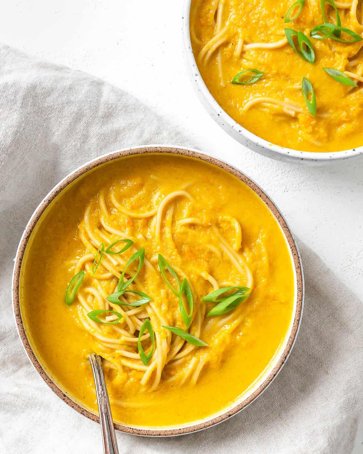 Karotten-Curry-Suppe mit Nudeln 2 Fertige Curry-Karotten-Suppe mit Nudeln auf weißem Untergrund