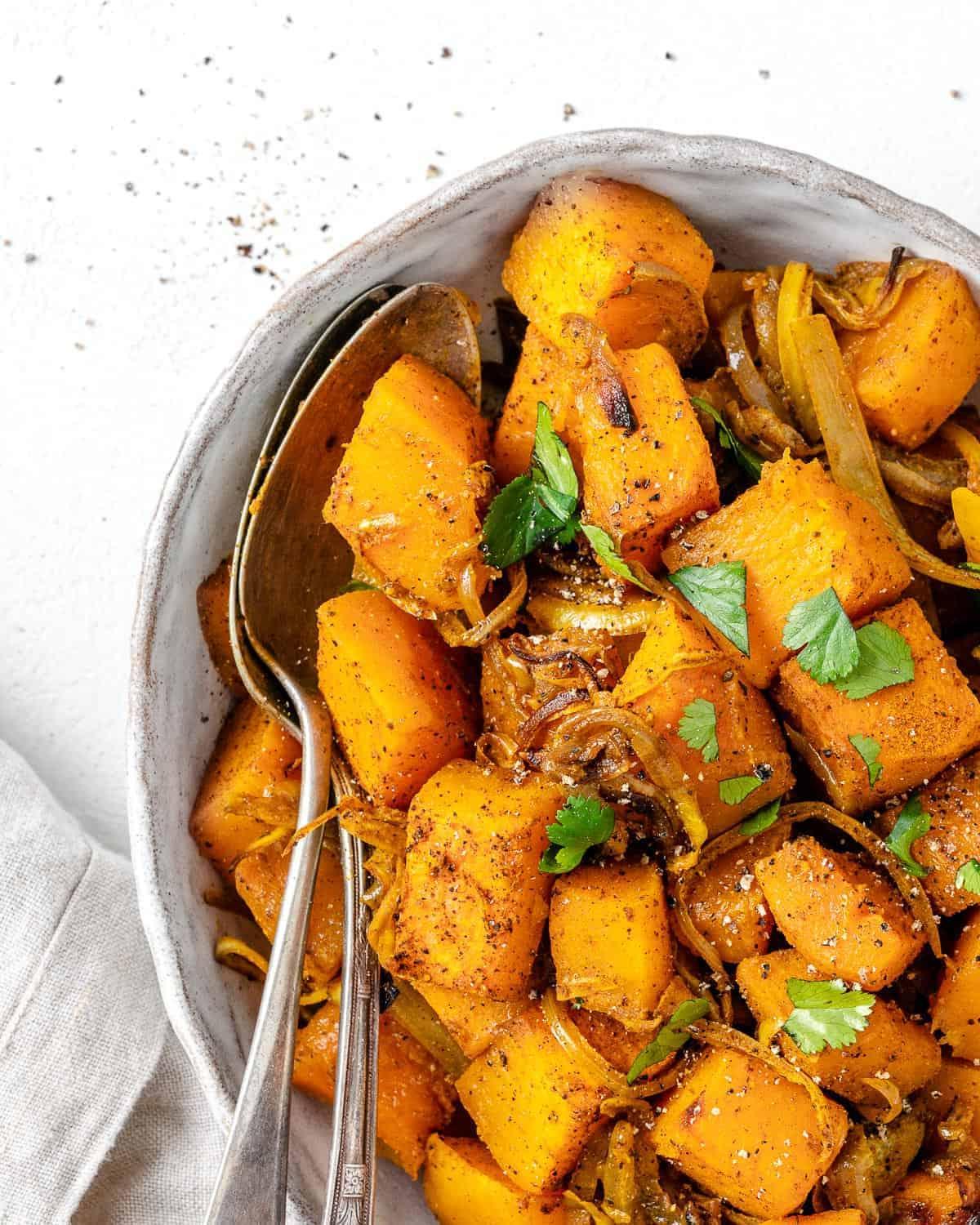 Fertig gerösteter Butternut-Kürbis mit indischen Gewürzen und karamelisierten Zwiebeln auf einer Servierplatte vor weißem Hintergrund