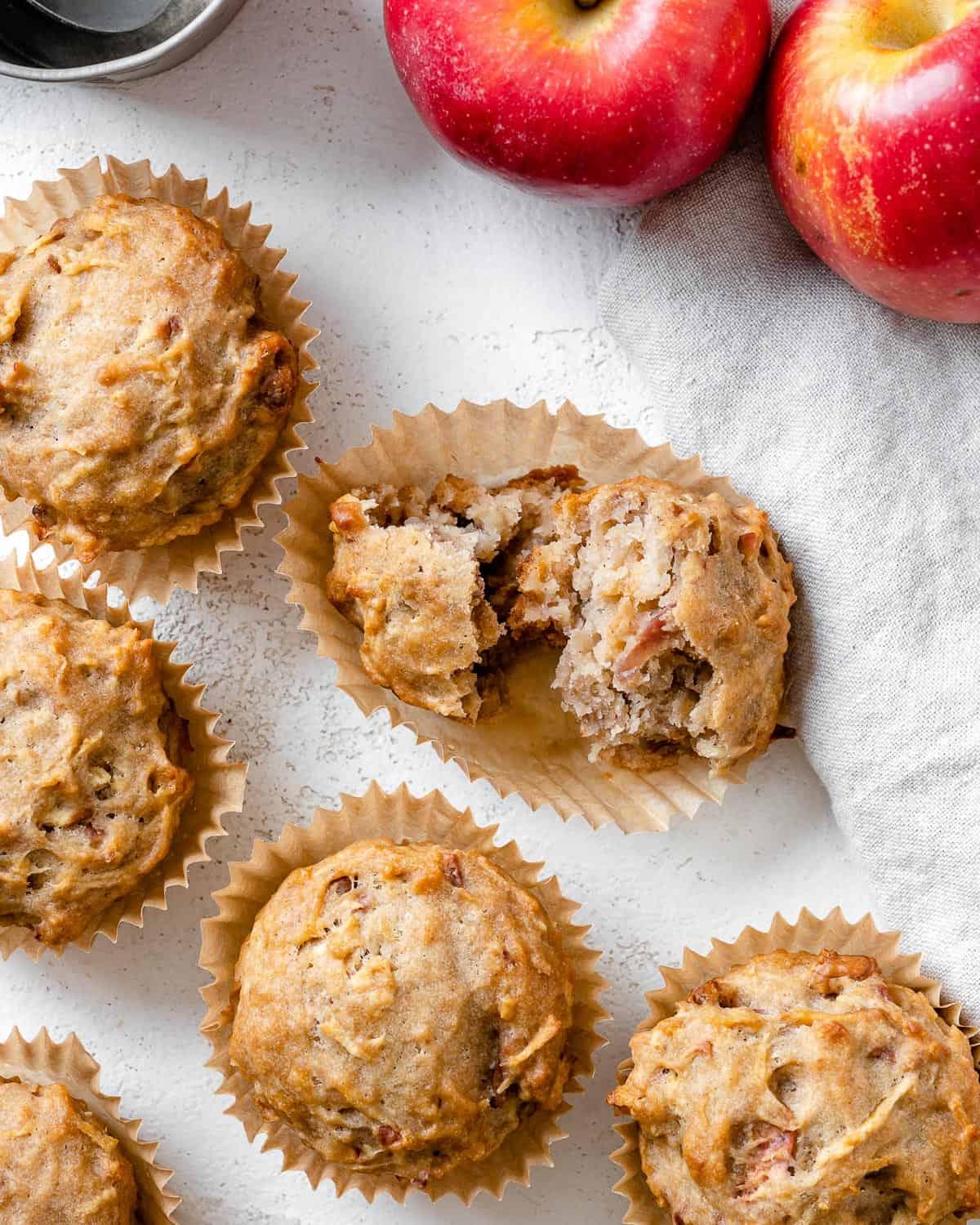 Einfache Vegane Apfelmuffins 2 Mehrere fertig gebackene vegane Apfelmuffins auf einer weißen Oberfläche ausgebreitet
