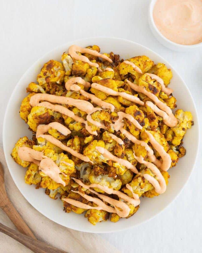 **Unkomplizierter Knusper-Blumenkohl** 2 Ein Teller mit knusprigem, unkompliziertem Blumenkohl, beträufelt mit Tahini-Sauce.