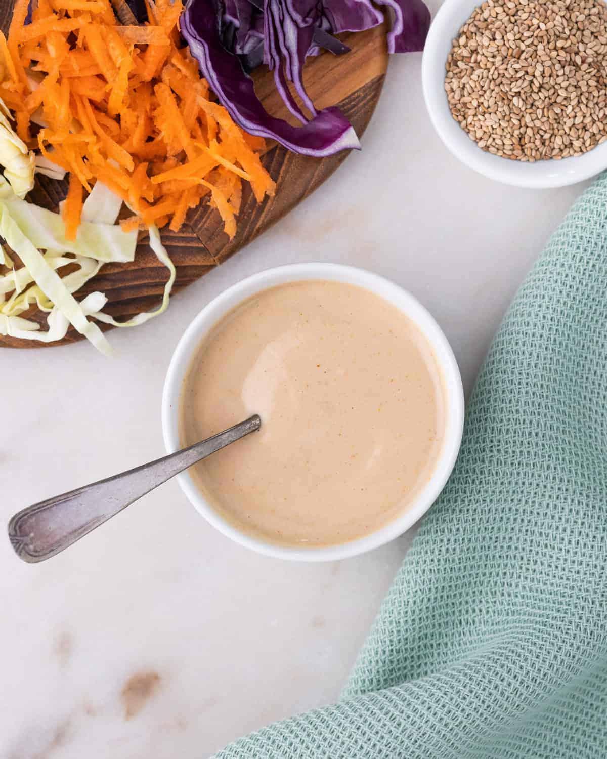 completed slaw dressing in a white bowl with a utensil in it along with veggies in the background