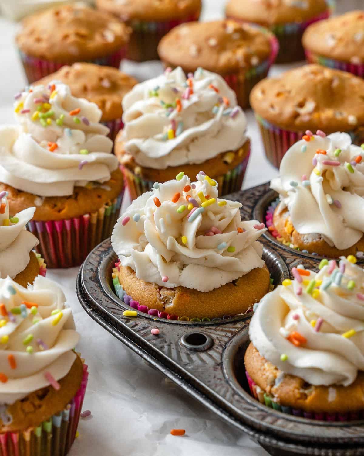 Vegane Konfetti-Cupcakes 2 Fertige vegane Funfetti Cupcakes auf einer weißen Oberfläche und in einer Muffinform