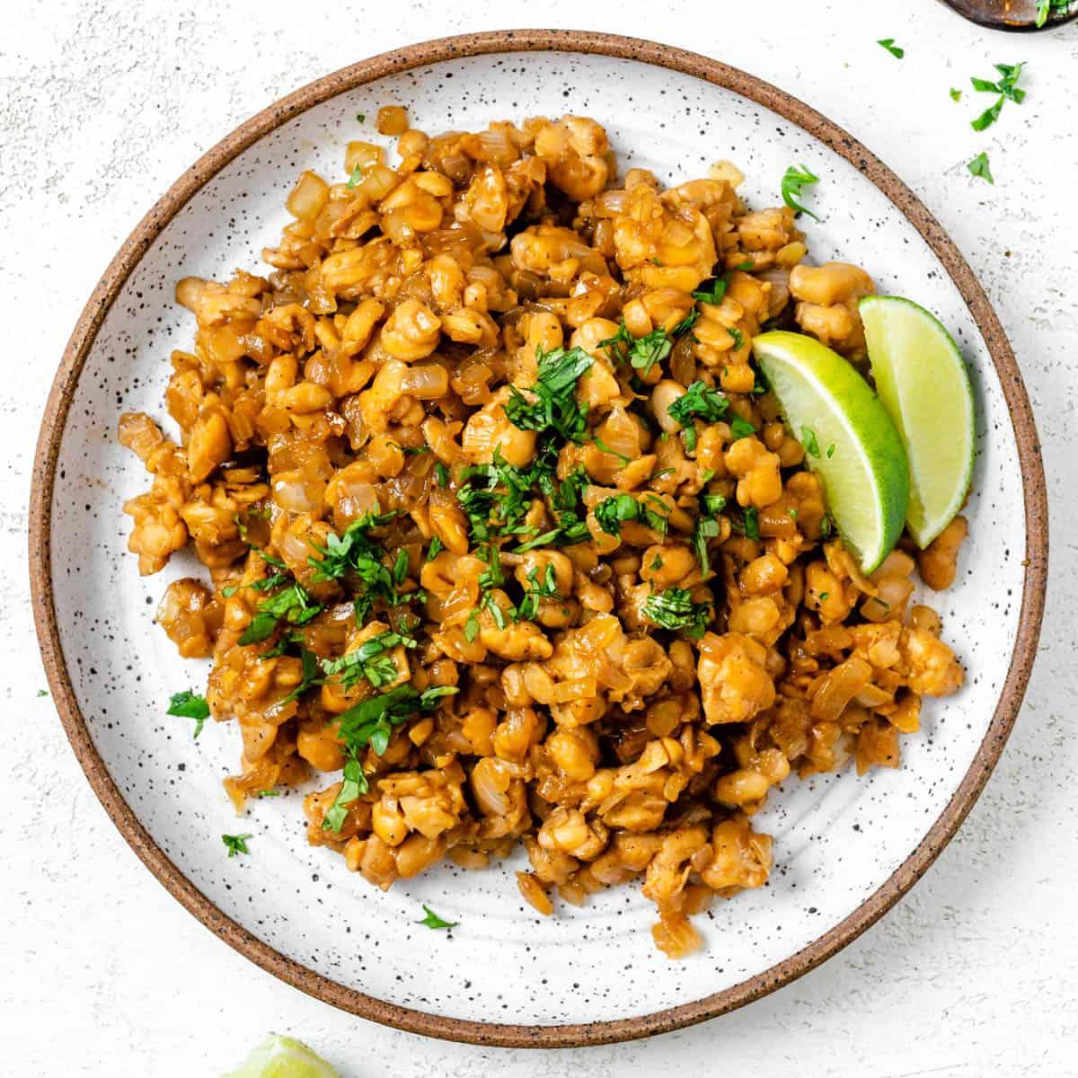 Pfannengebratenes Tempeh mit Ingwer-Sojasauce 2 Fertig gebratenes Tempeh mit Ingwer-Soja-Sauce auf einem Teller vor hellem Hintergrund
