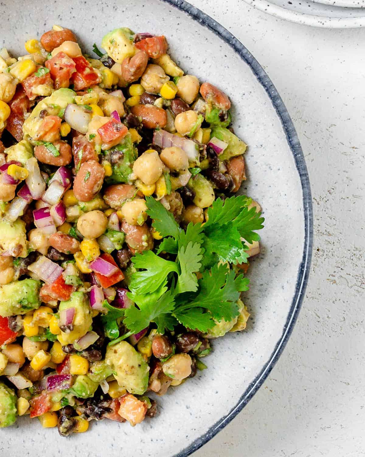 Fertiges Texas Caviar [Avocado-Mais-Bohnen-Salat] auf einem weißen Teller vor hellem Hintergrund