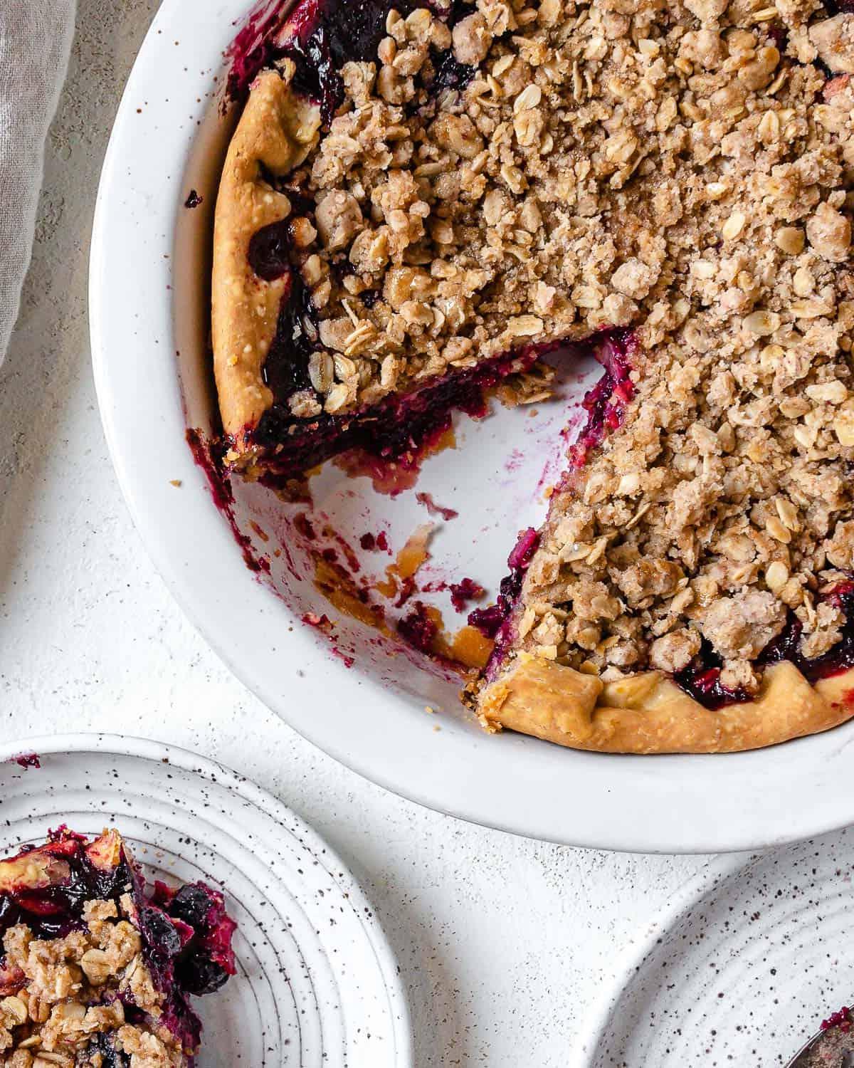 completed Mixed Berry Crumb Pie with a piece plated on a small white plate