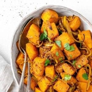 Fertig gerösteter Butternut-Kürbis mit indischen Gewürzen und karamelisierten Zwiebeln auf einer Servierplatte vor weißem Hintergrund