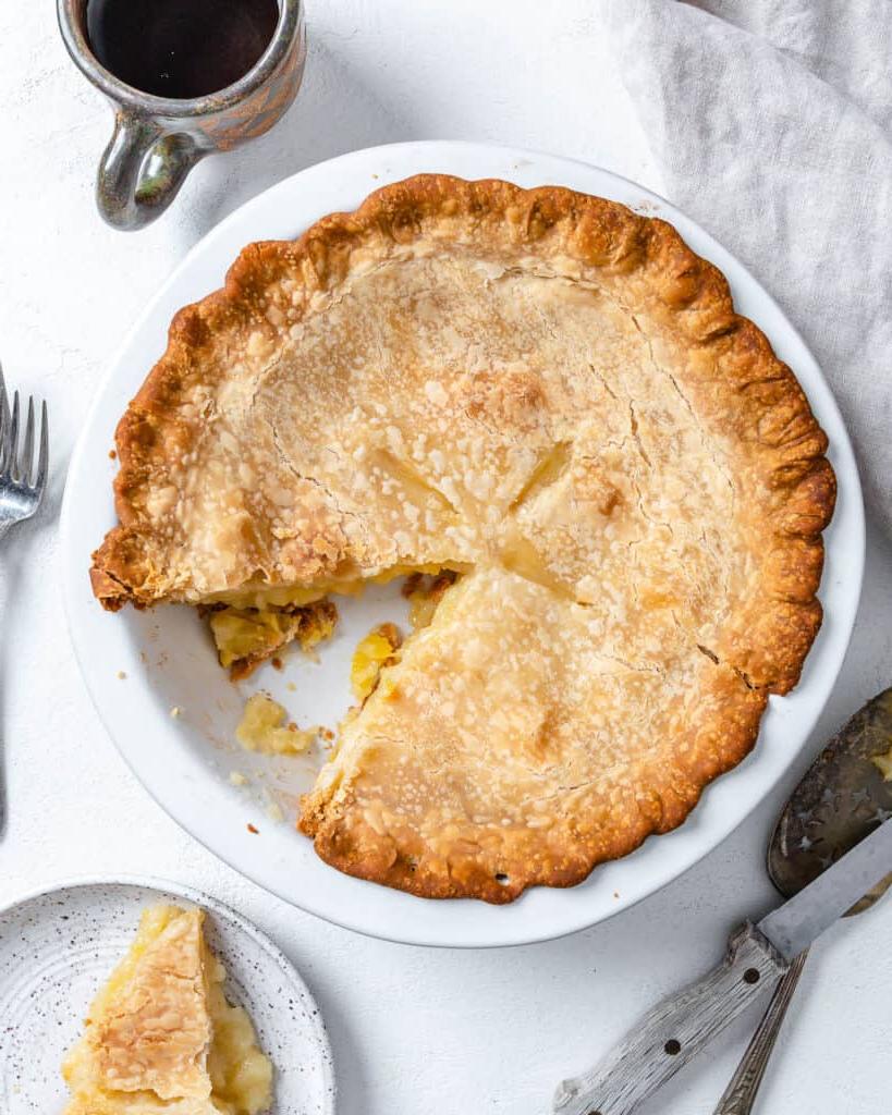 Veganer Kokos-Ananas-Kuchen 11 Fertiger Veganer Kokos-Ananas-Kuchen in Kuchenform mit einem fehlenden Stück vor weißem Hintergrund