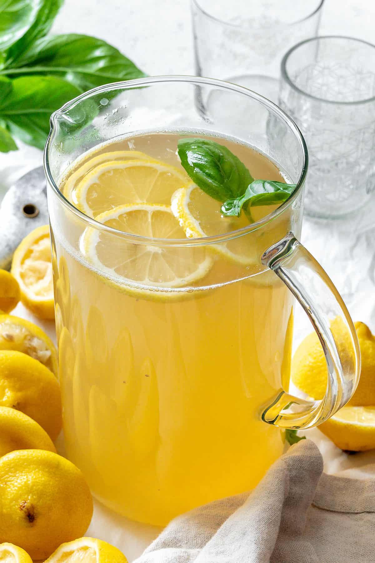 Fertige Basilikum-Limonade in einem Glas mit Zutaten im Hintergrund