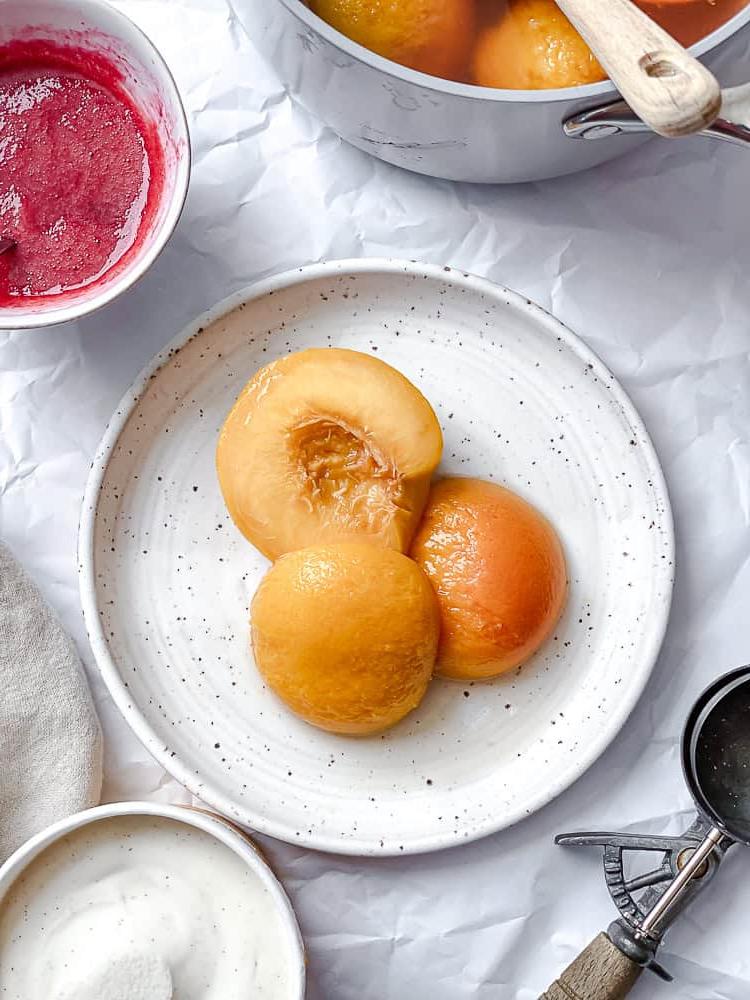 Peach Melba 12 Drei pochierte Pfirsichhälften liegen auf einem Teller angerichtet.