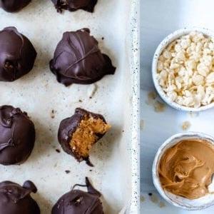 Vegane Schoko-Erdnussbutter-Kugeln ohne Backen mit Reis-Crispies 12 Mehrere fertige Erdnussbutter-Bonbons, eines davon mit einem Bissen