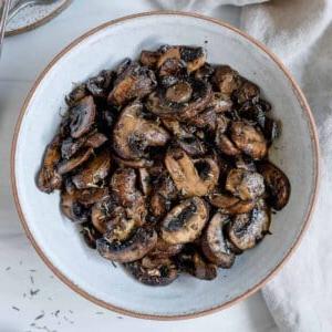 **Pilze im Ofen rösten (+ Geschmacksvariationen)** 12 completed simple roasted mushrooms on a white plate against a white background