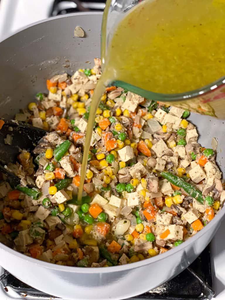 process shot of veggie broth being added to pan
