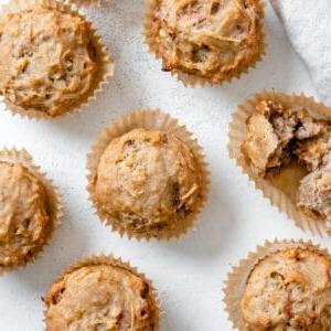 Einfache Vegane Apfelmuffins 12 Mehrere fertig gebackene vegane Apfelmuffins auf einer weißen Oberfläche ausgebreitet