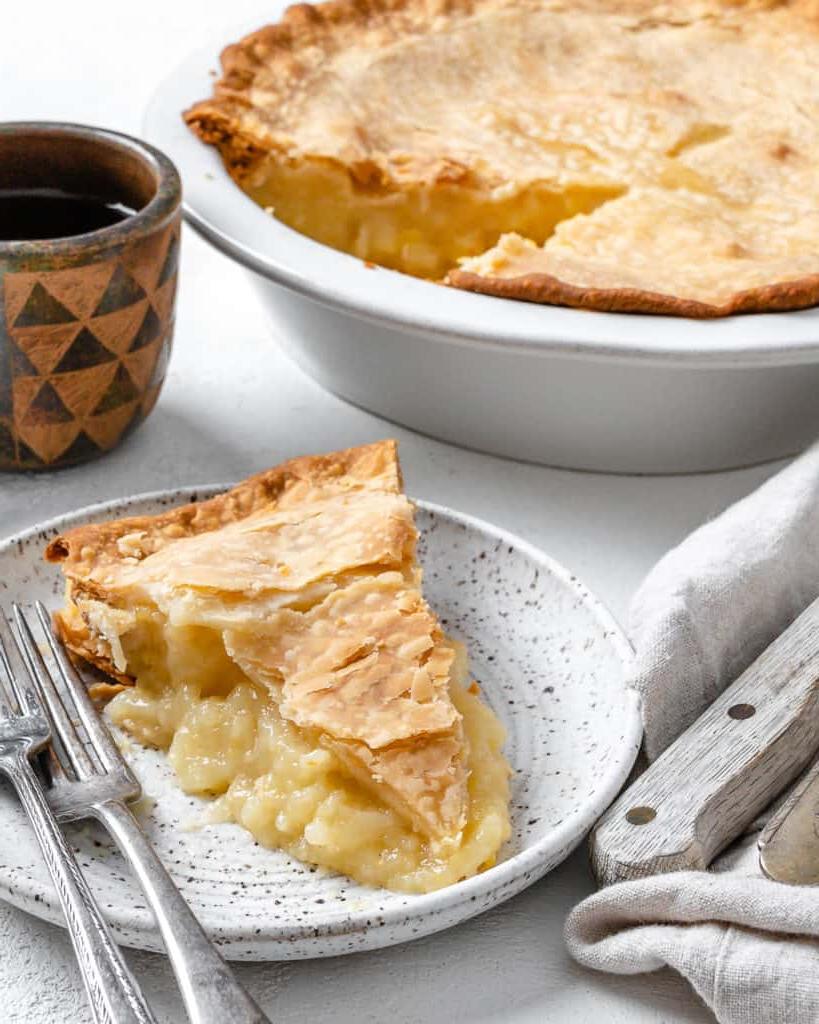 Veganer Kokos-Ananas-Kuchen 12 Fertiger Veganer Kokos-Ananas-Kuchen in Kuchenform mit einer Scheibe auf einem separaten weißen Teller