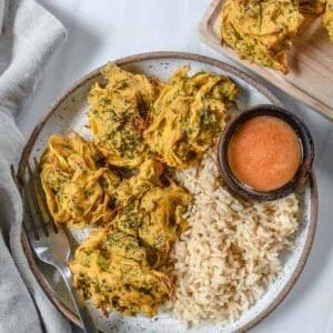 Brokkoli-Zwiebel-Pakora 12 Fertige Brokkoli- und Zwiebel-Pakora auf einem Teller mit Reis und einer Sauce angerichtet