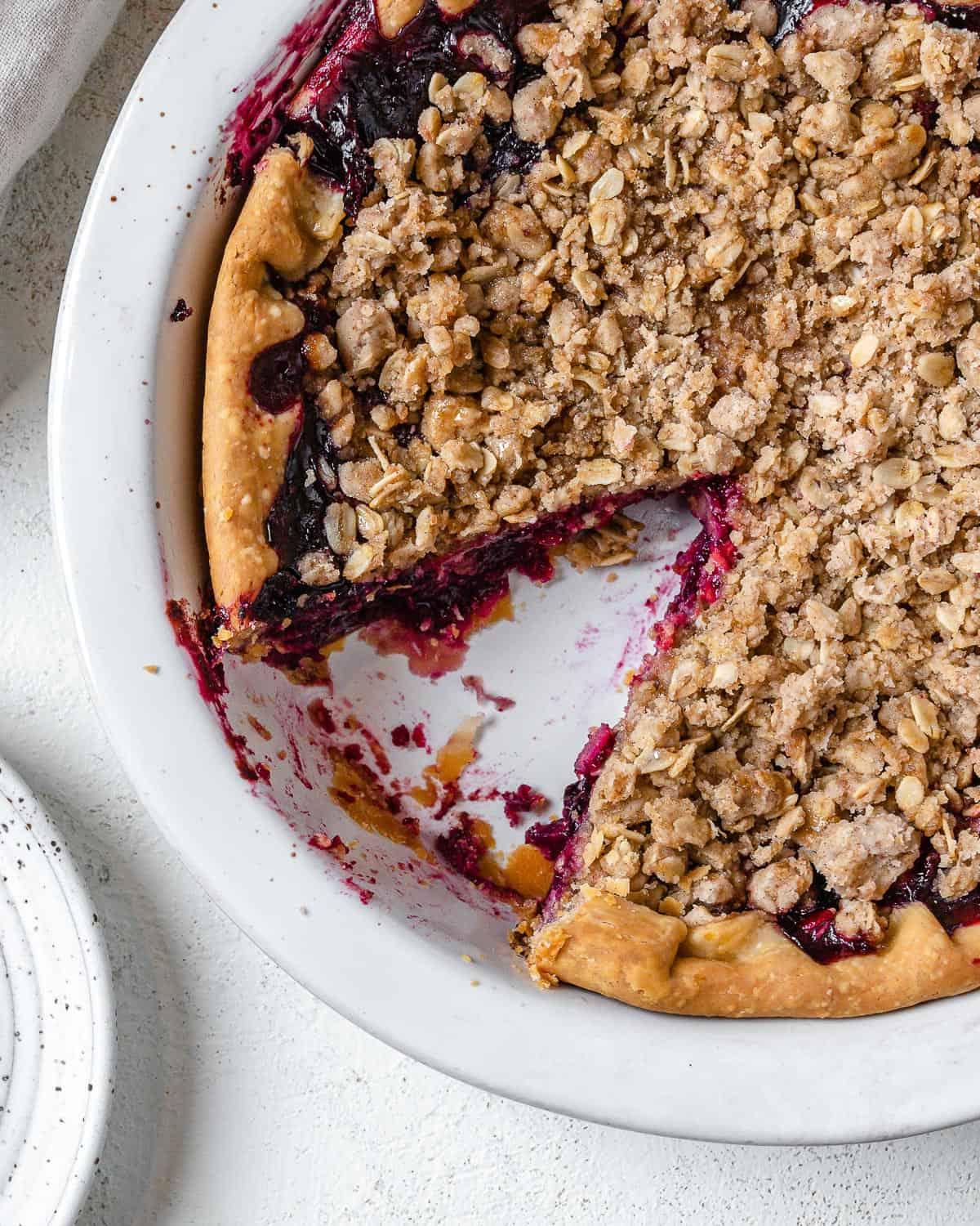 completed Mixed Berry Crumb Pie with a piece plated on a small white plate
