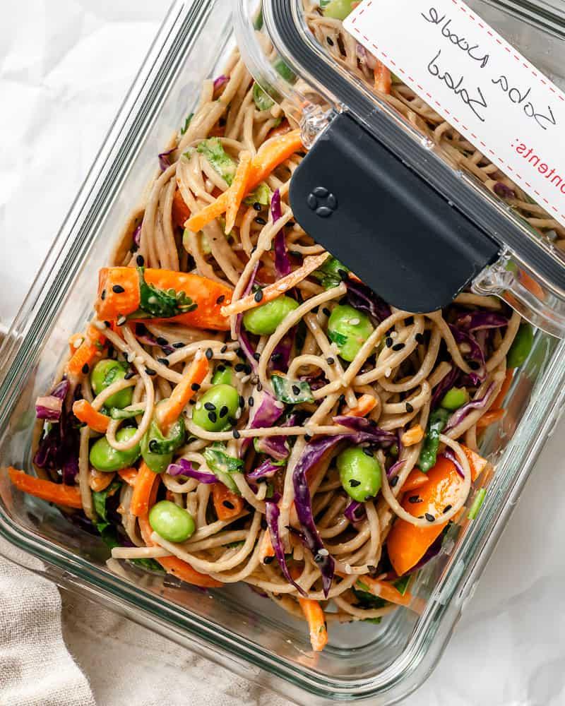 a serving of soba noodle salad in a glass container with a lid on top labeled "soba noodle salad".