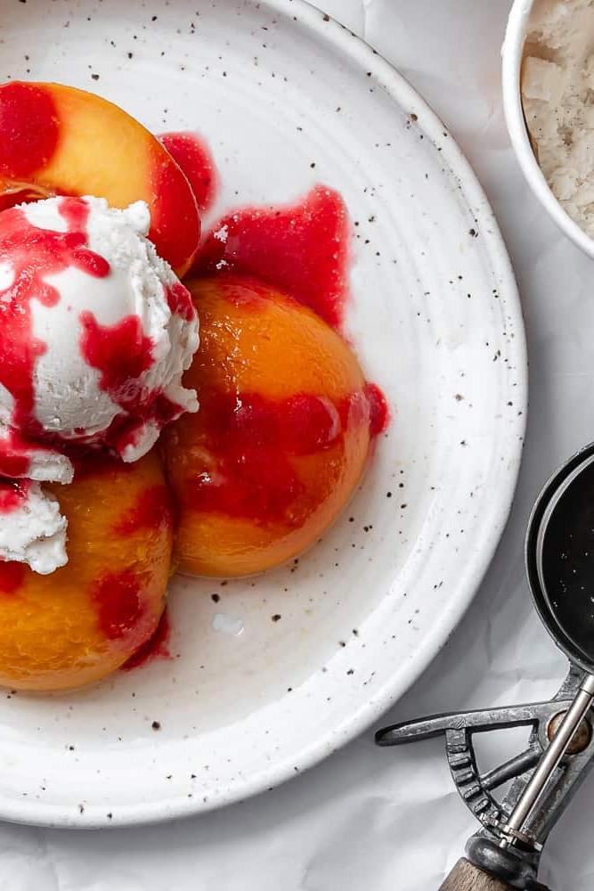 Peach Melba 13 Pochierte Pfirsiche mit Himbeersauce und Eiscreme auf einem Teller, nahaufnahme.