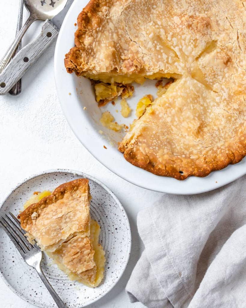 Veganer Kokos-Ananas-Kuchen 13 Fertiger Veganer Kokos-Ananas-Kuchen in Kuchenform mit einer Scheibe auf einem separaten weißen Teller