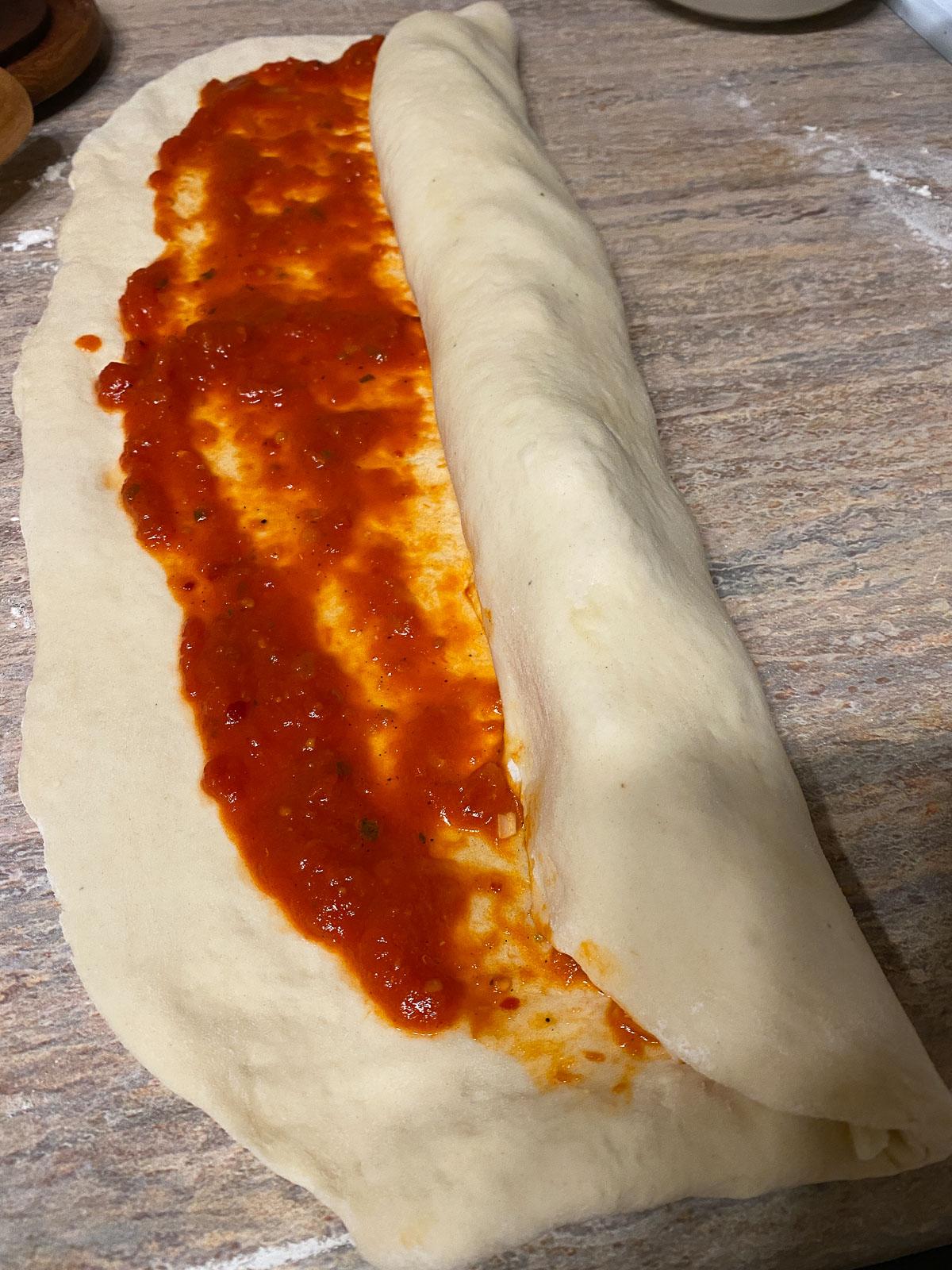 Vegane Pizzaröllchen 13 process of forming pizza roll against a light brown surface