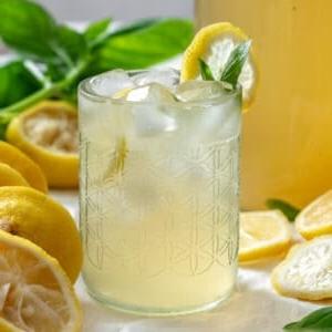 Fertige Basilikum-Limonade in einem Glas mit Zutaten im Hintergrund