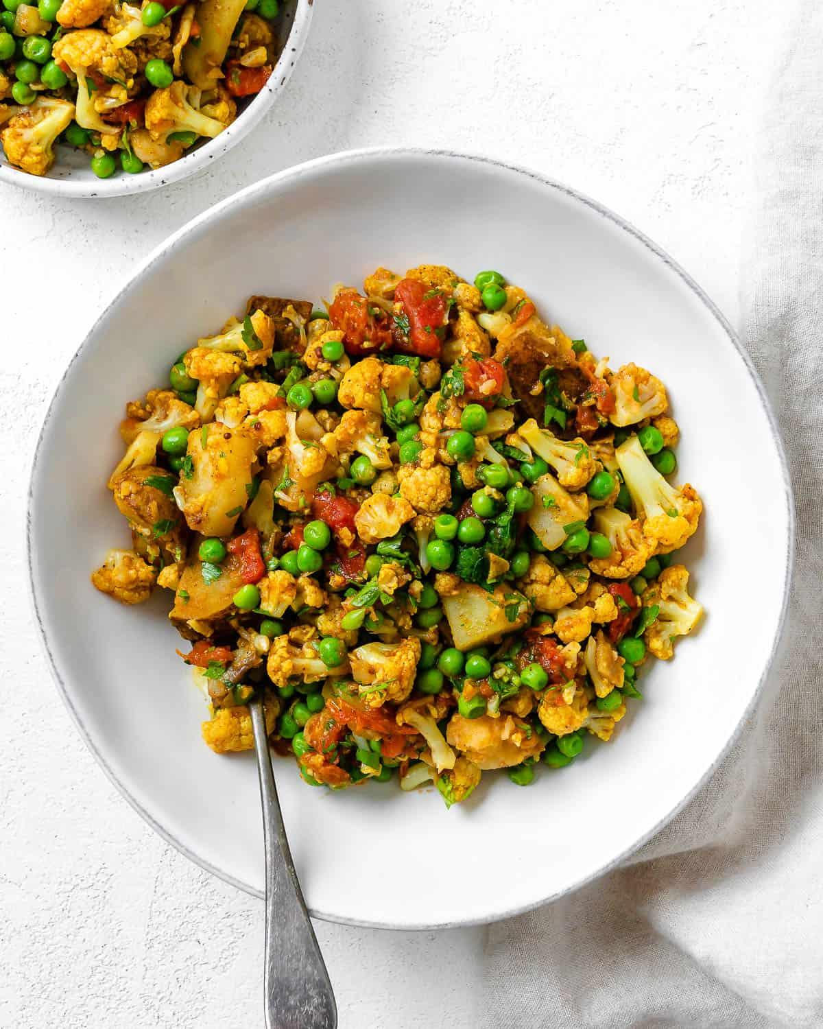 30 einfache vegane Kartoffelrezepte 15 Komplettes Aloo Gobi (Curry-Kartoffeln, Blumenkohl und Erbsen) in einer weißen Schüssel