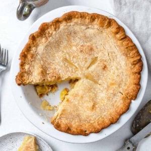 Veganer Kokos-Ananas-Kuchen 15 Fertiger Veganer Kokos-Ananas-Kuchen in Kuchenform mit einem fehlenden Stück vor weißem Hintergrund