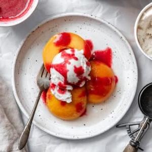 Peach Melba 16 Pochierte Pfirsiche mit Himbeersauce und Eiscreme auf einem Teller angerichtet.
