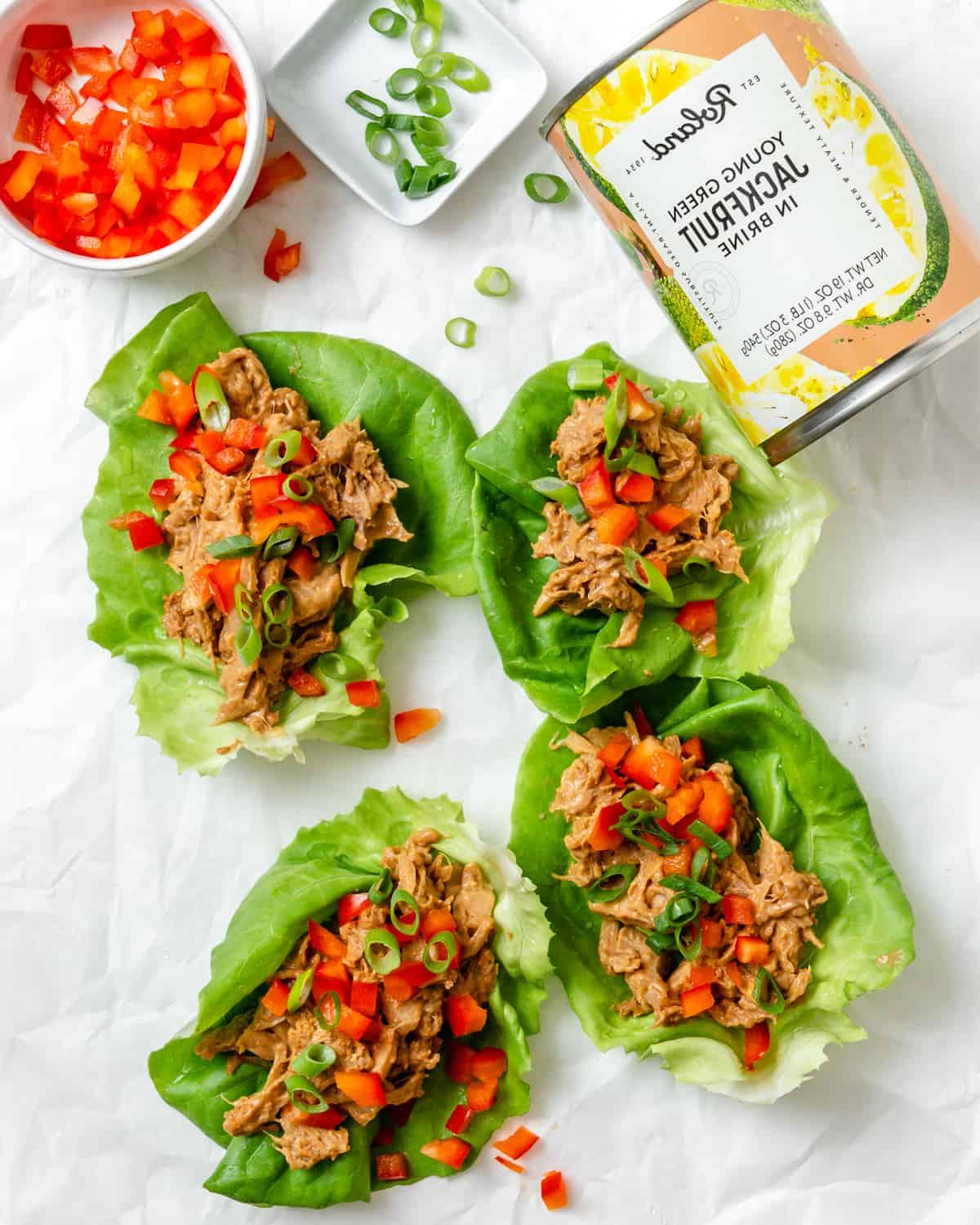 Jackfrucht-Salatwickel 16 Mehrere fertige Jackfrucht-Salat-Wraps auf einer weißen Fläche mit einer Jackfrucht-Dose im Hintergrund