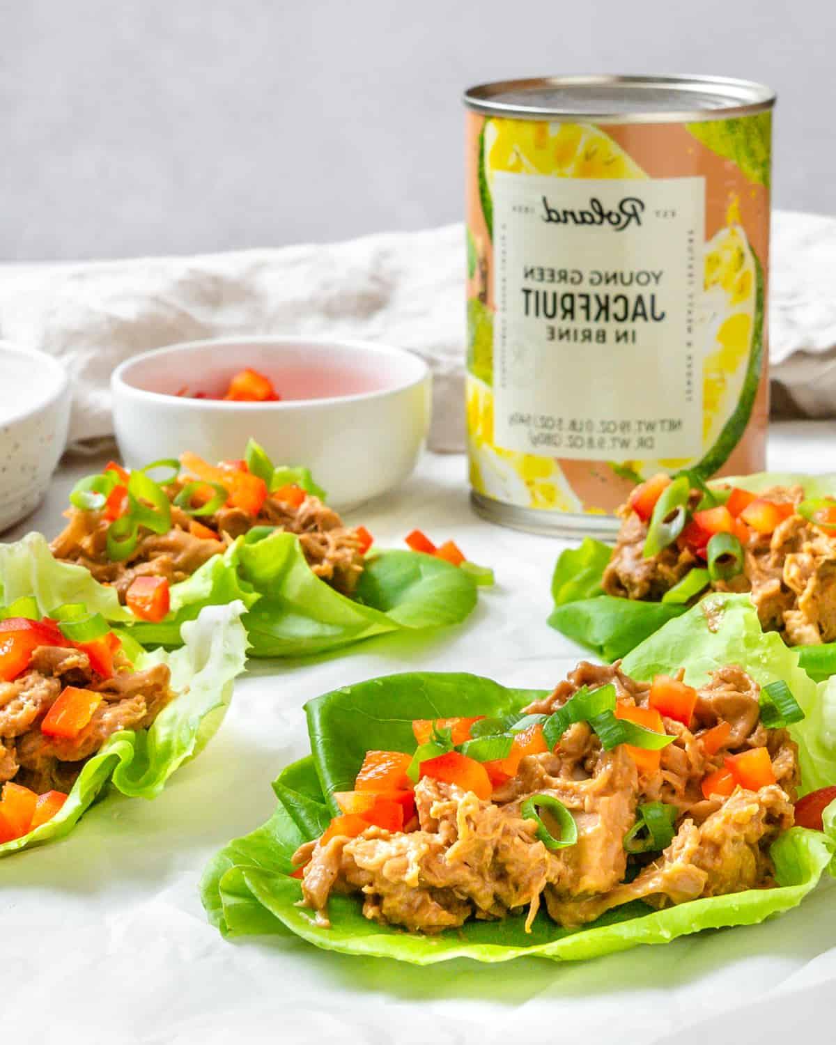 Jackfrucht-Salatwickel 17 Mehrere fertige Jackfrucht-Salat-Wraps auf einer weißen Fläche mit einer Jackfrucht-Dose im Hintergrund