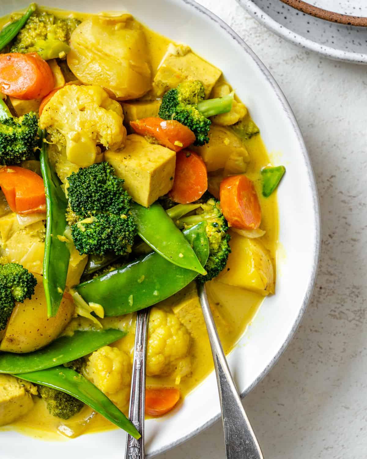 30 einfache vegane Kartoffelrezepte 17 Fertiges Einfaches Tofu-Gemüse-Kokos-Curry in einer Schüssel auf weißem Hintergrund