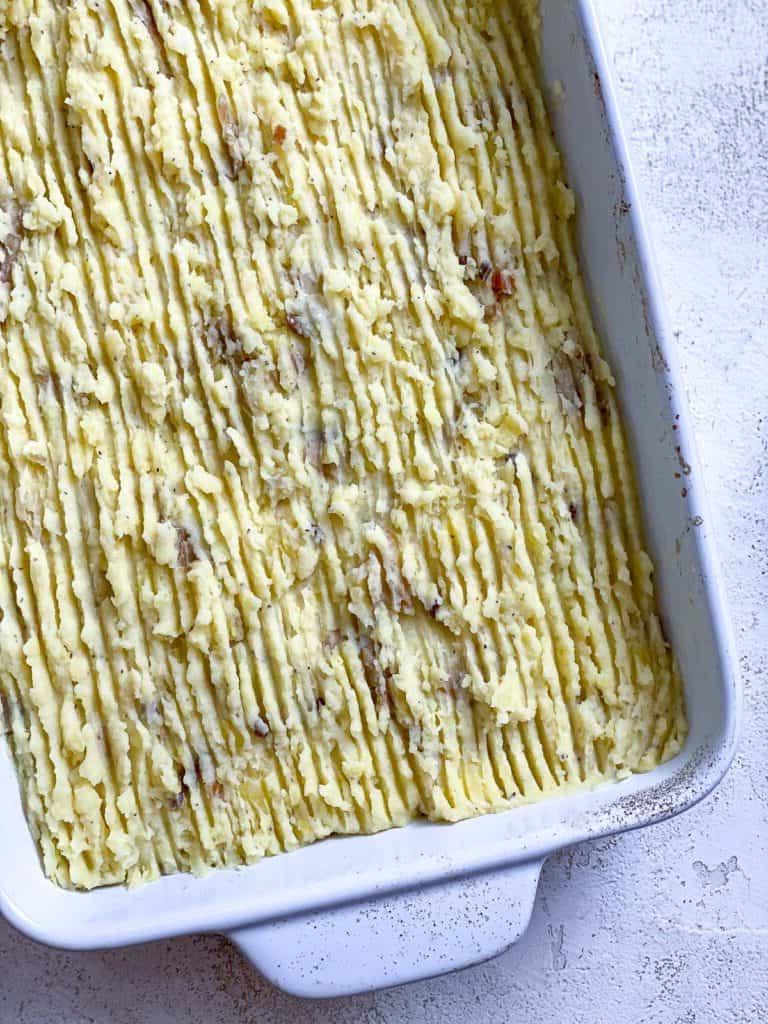 Veganer Linsen-Hirtenkuchen 20 Kartoffelpüree-Schicht wird auf die Linsenfüllung in der Auflaufform aufgetragen
