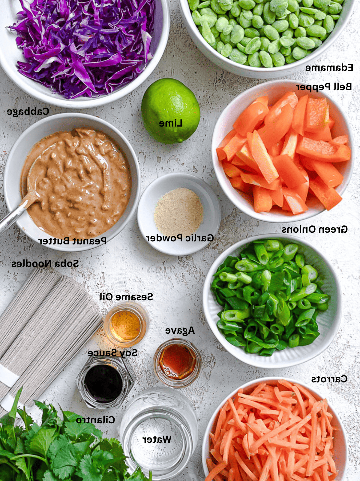 ingredients for soba noodle salad in individual white bowls with labels.