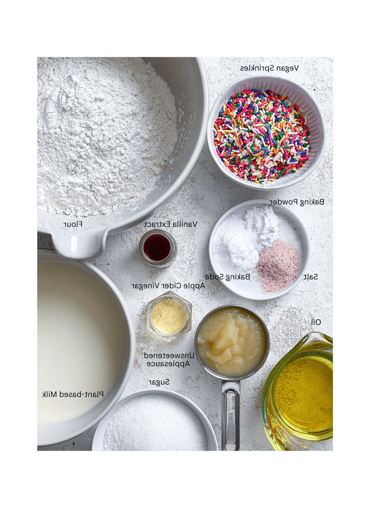 Zutaten für veganen Geburtstagskuchen [Funfetti Kuchen] auf einer weißen Oberfläche
