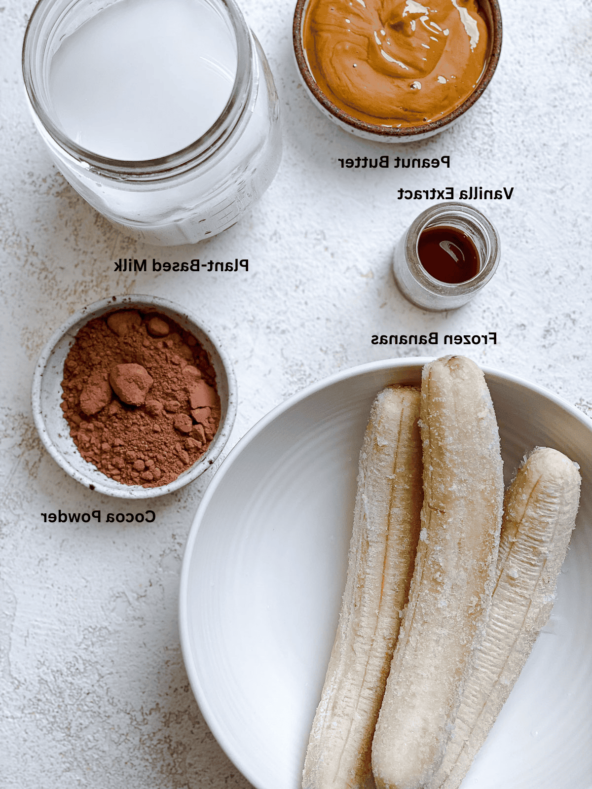 Schokoladen-Bananen-Milchshake 3 Zutaten für den Schoko-Bananen-Milchshake, abgemessen auf einer weißen Oberfläche