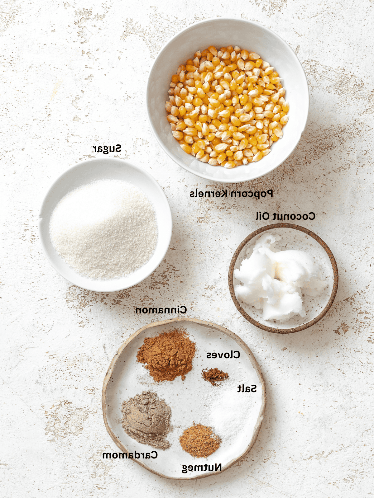 Für Chai-Popcorn abgemessene Zutaten auf einer weißen Fläche.