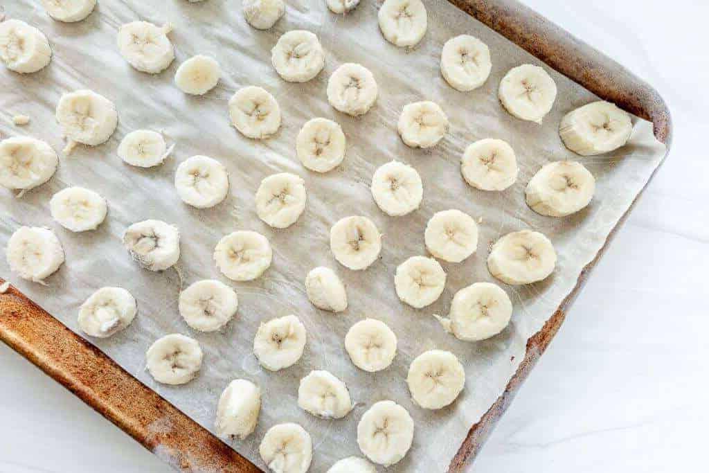 Gefrorene Bananenscheiben auf einem mit Backpapier ausgelegten Backblech.