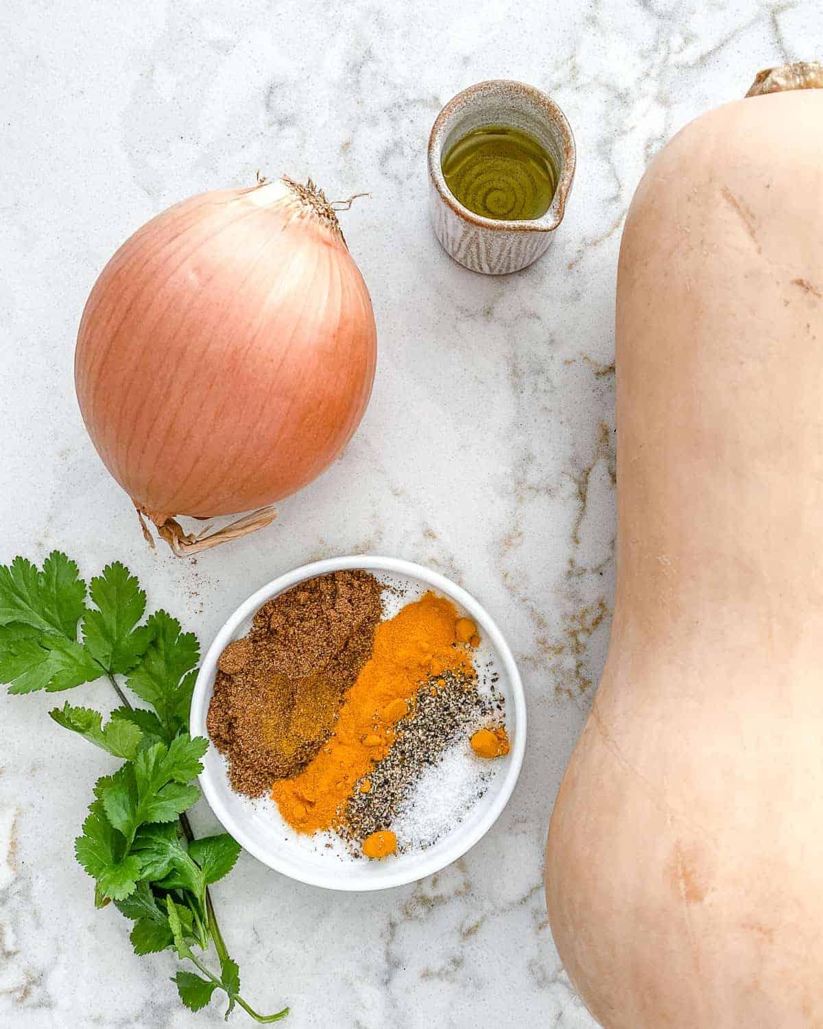 Zutaten für gerösteten Butternut-Kürbis mit indischen Gewürzen und karamelisierten Zwiebeln auf einer weißen Marmoroberfläche