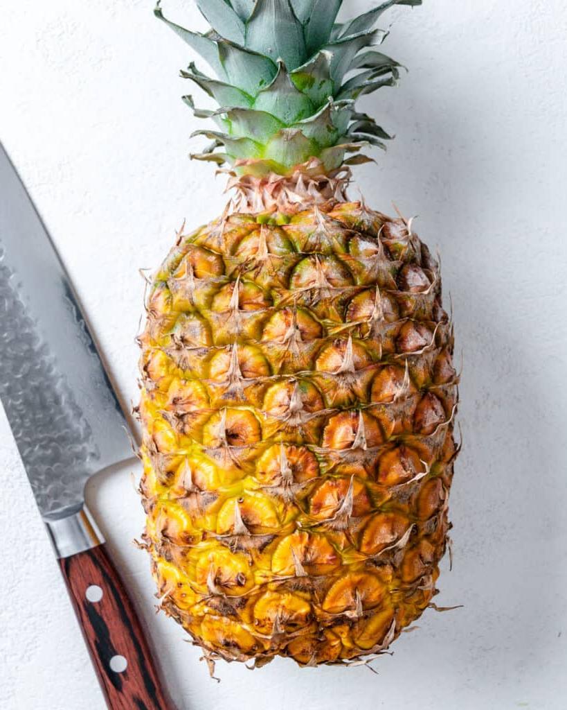 Veganer Kokos-Ananas-Kuchen 3 Ganze Ananas und Schneidemesser vor weißem Hintergrund