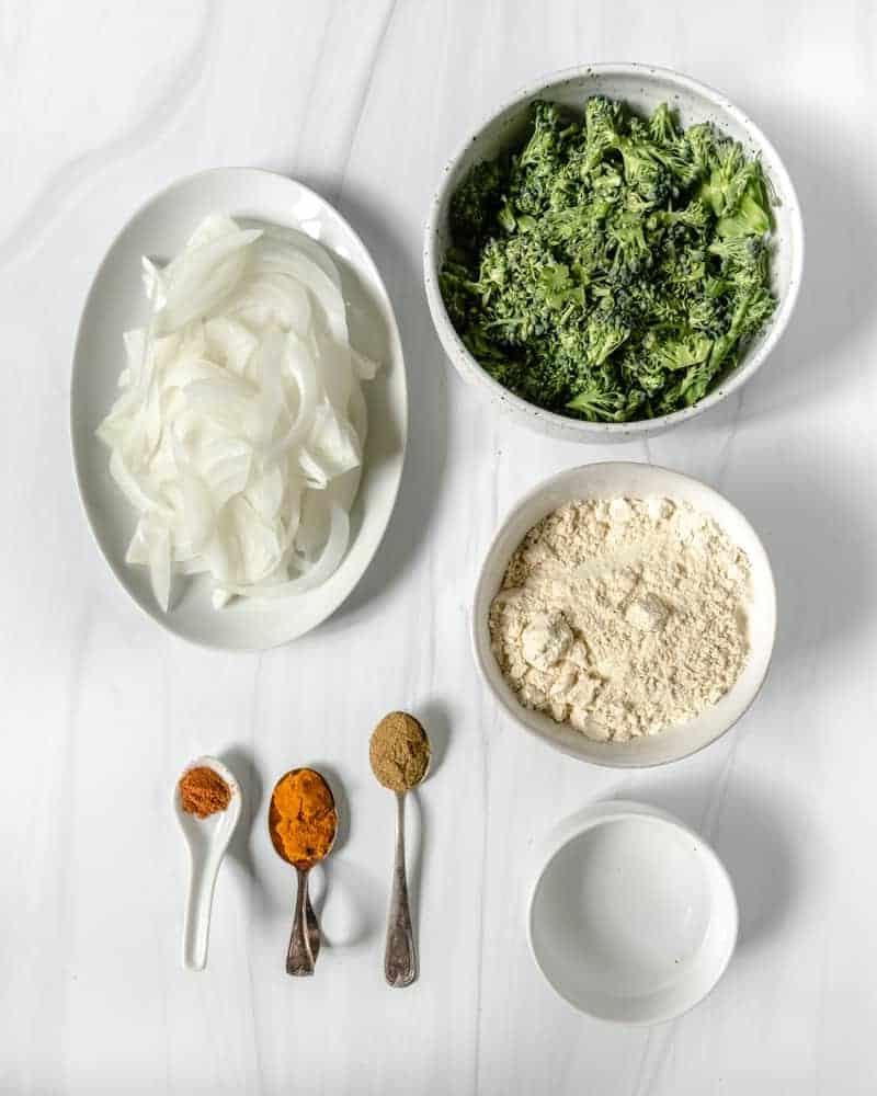 Zutaten für Brokkoli- und Zwiebel-Pakora auf einer weißen Oberfläche
