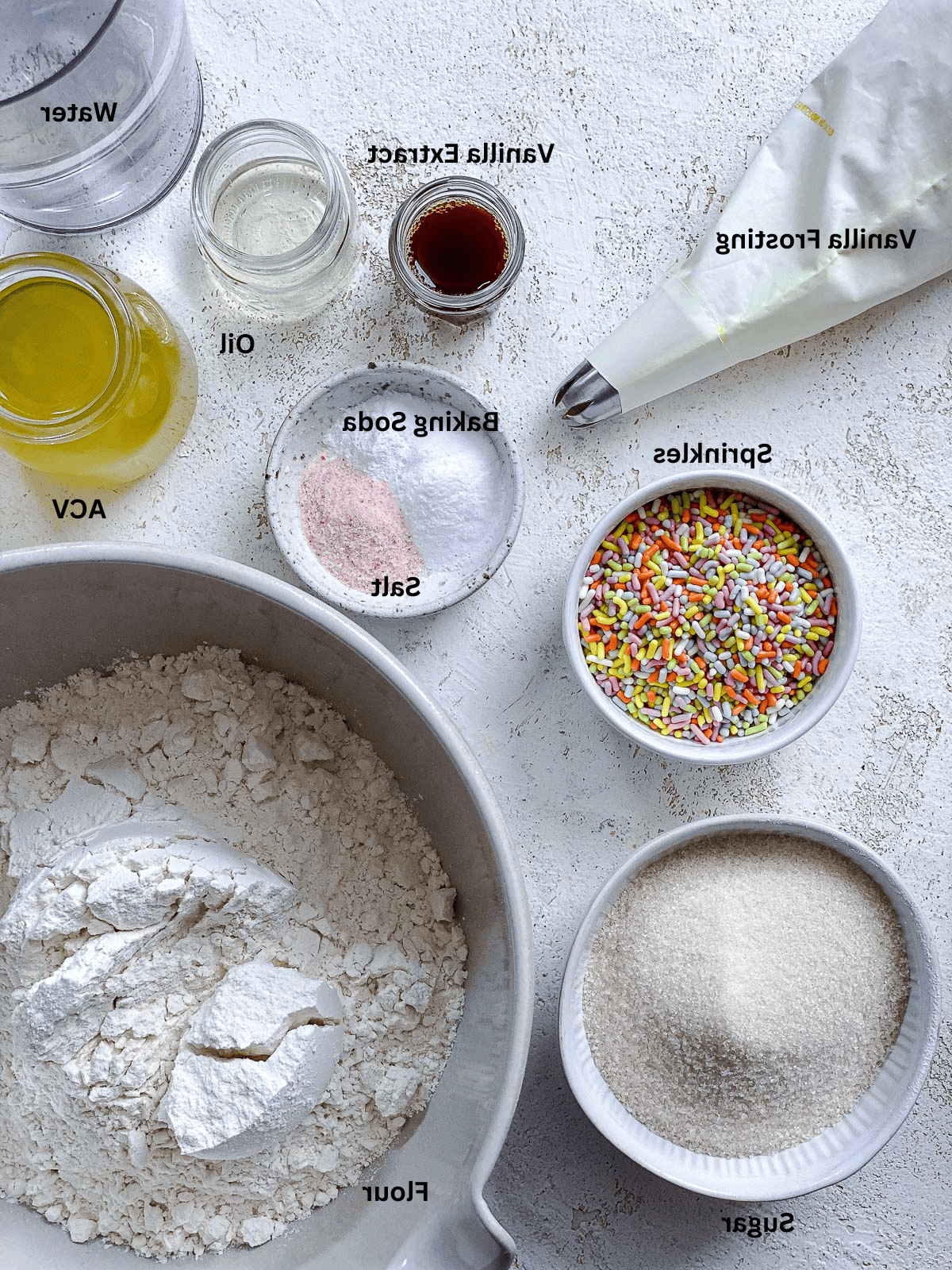 Vegane Konfetti-Cupcakes 3 Eine Auswahl an Zutaten für vegane Cupcakes, darunter Mehl, Zucker, Öl, Vanilleextrakt und Streusel.