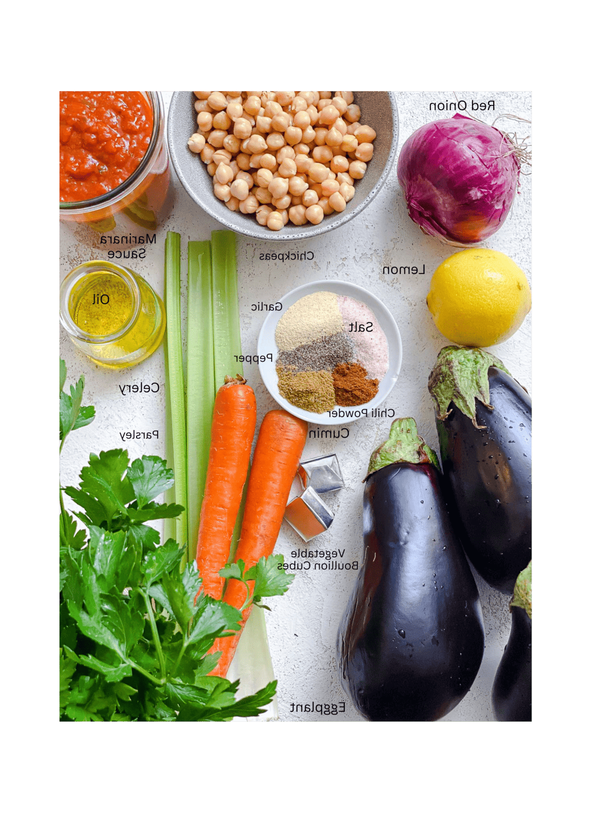 Zutaten für Auberginen-Eintopf mit Tomaten und Kichererbsen auf einer weißen Oberfläche