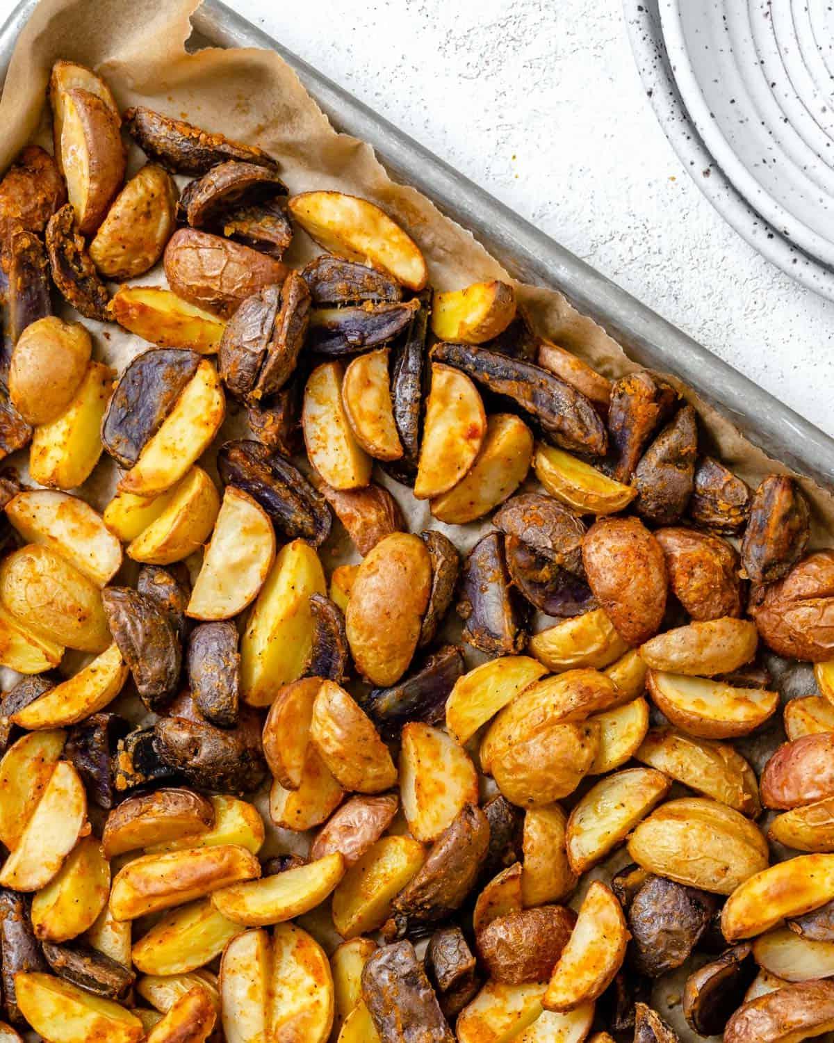 30 einfache vegane Kartoffelrezepte 26 Fertige knusprige lila Kartoffeln auf einem Backblech auf weißem Hintergrund