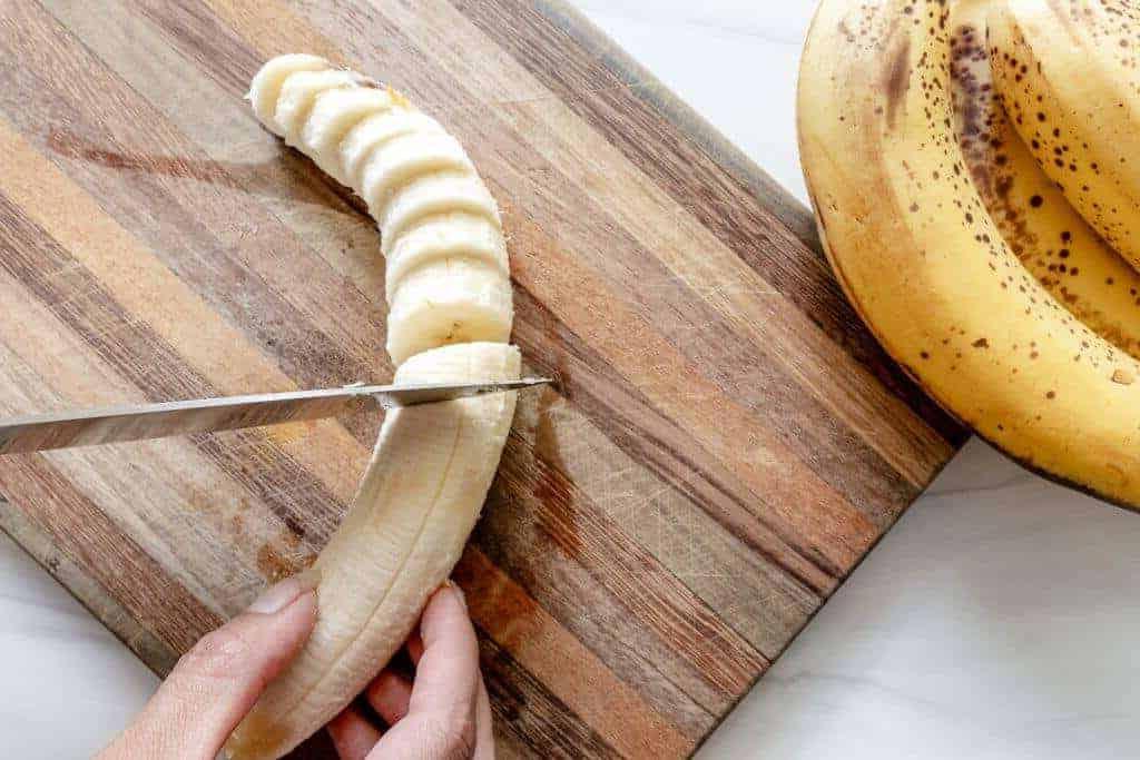 Eine Banane wird auf einem Holzbrett geschnitten.